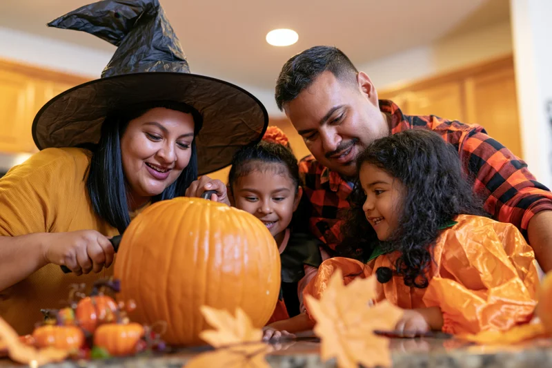 Latino family carving a large pumpkin together in a home kitchen