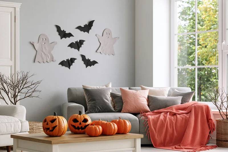 Halloween-decorated living room with paper ghost and bat cutouts on the wall and pumpkins on the coffee table