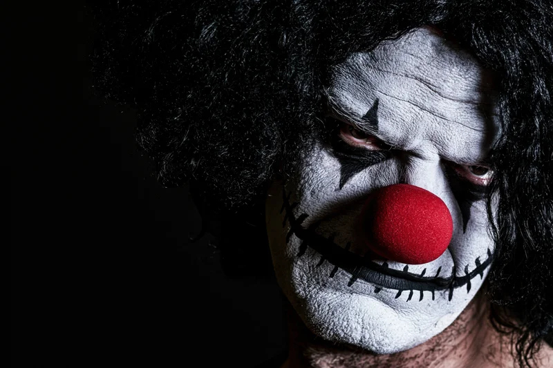 Man with sinister clown makeup and red foam nose in dark closeup
