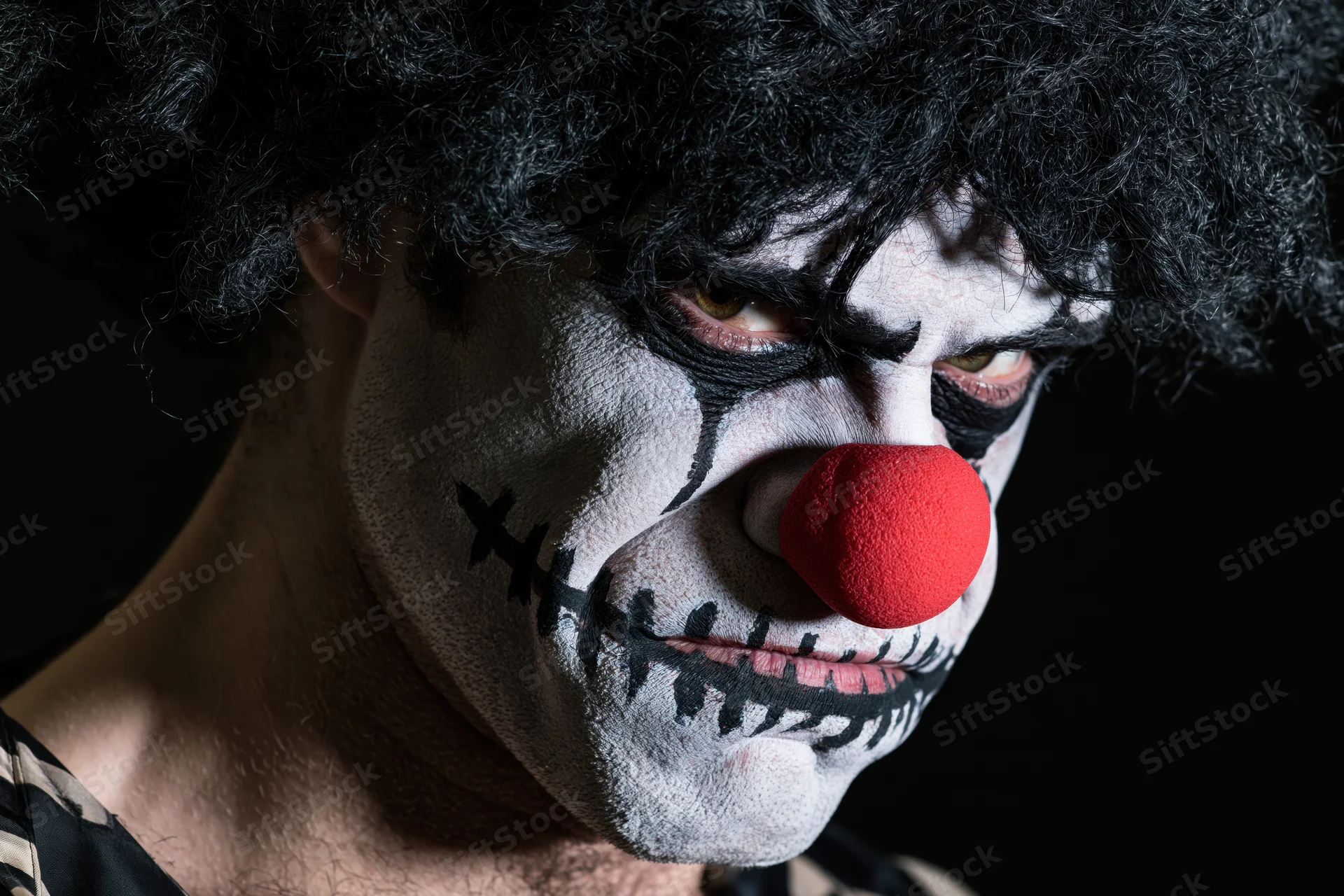 Man with sinister clown makeup and red foam nose in dark closeup