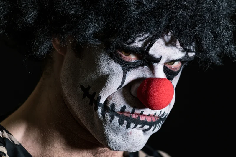Man with sinister clown makeup and red foam nose in dark closeup