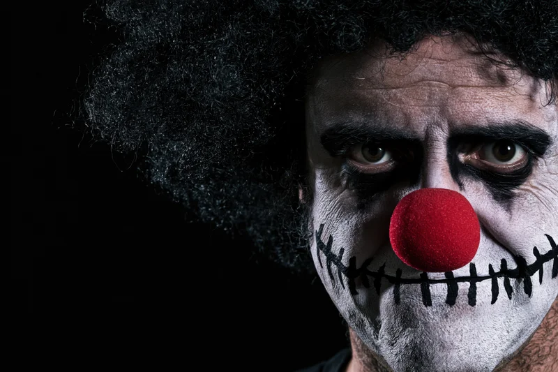 Man with sinister clown makeup and red foam nose in dark closeup