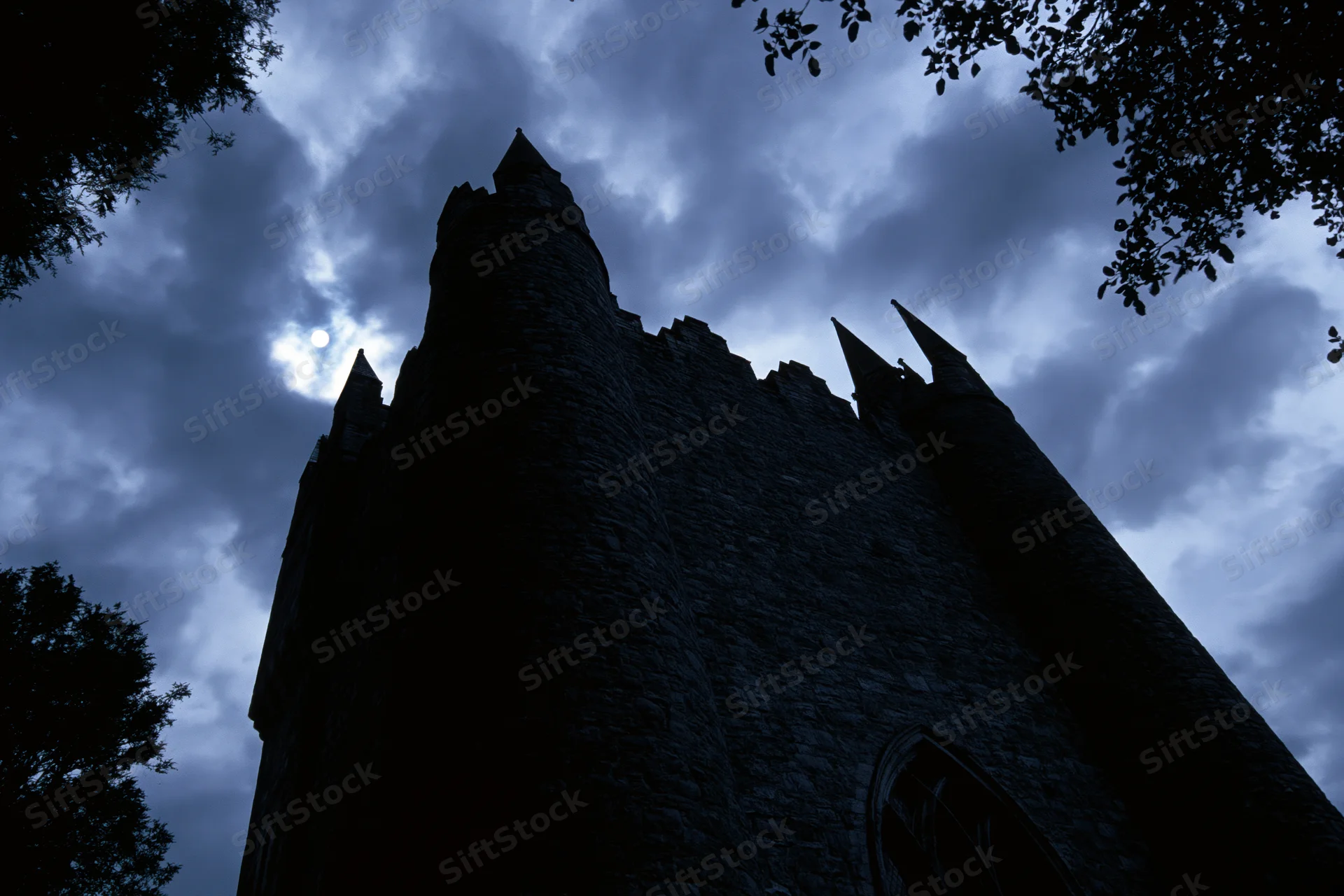 Dark silhouette of a medieval stone castle with pointed towers against a cloudy night sky