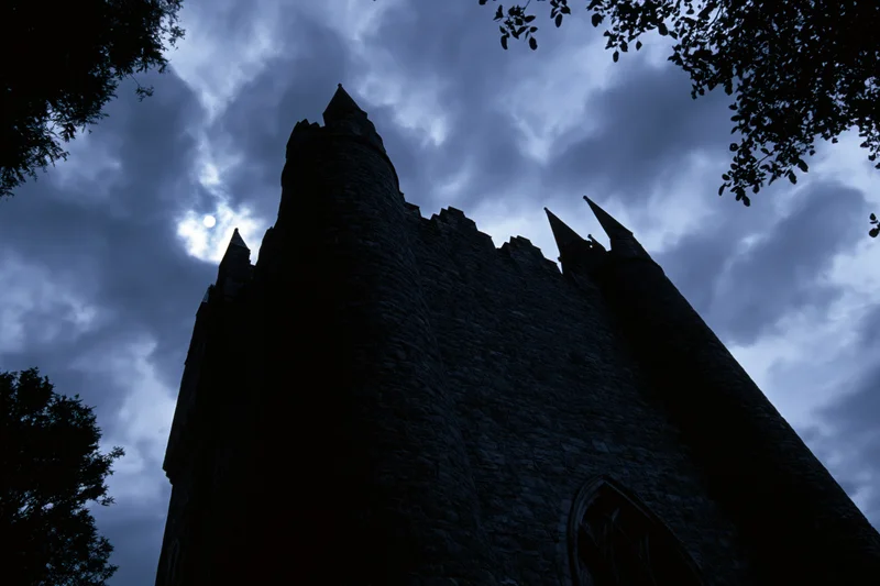 Dark silhouette of a medieval stone castle with pointed towers against a cloudy night sky