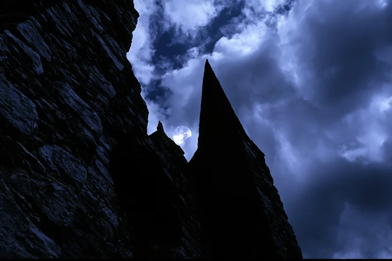 Medieval stone castle with pointed towers silhouetted against a cloudy night sky with moonlight