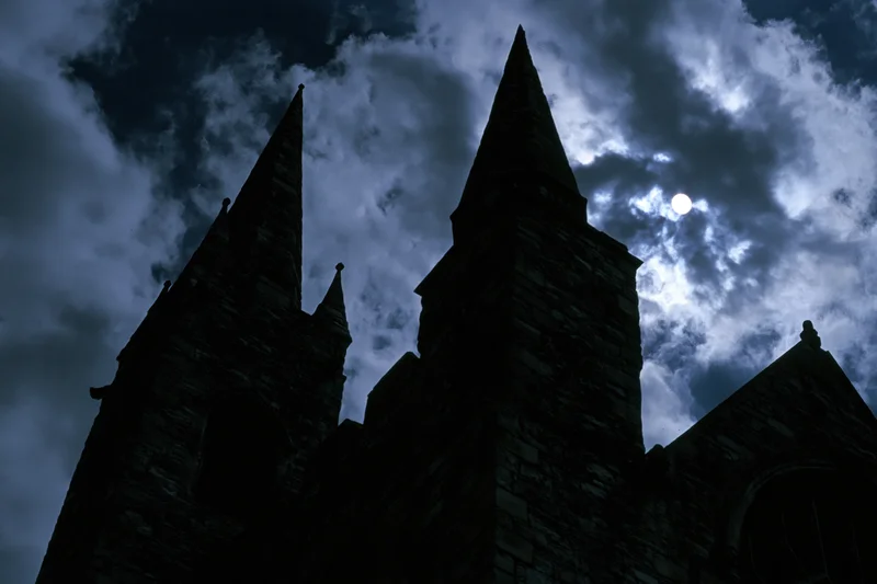 Medieval stone castle with pointed towers silhouetted against a cloudy night sky with moonlight