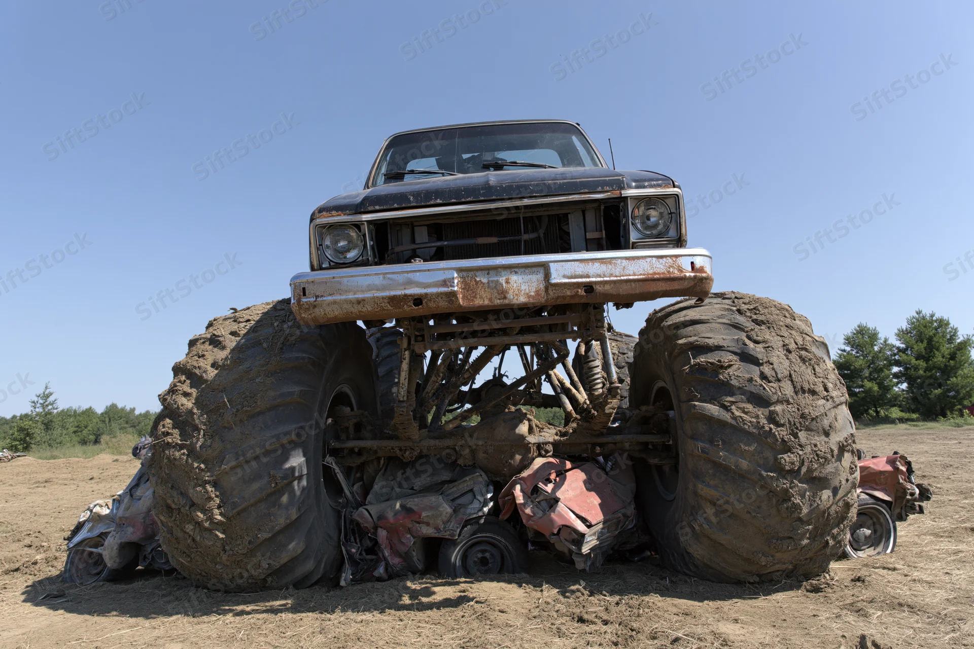 Monster truck crushing wrecked cars in a dirt field under clear sky
