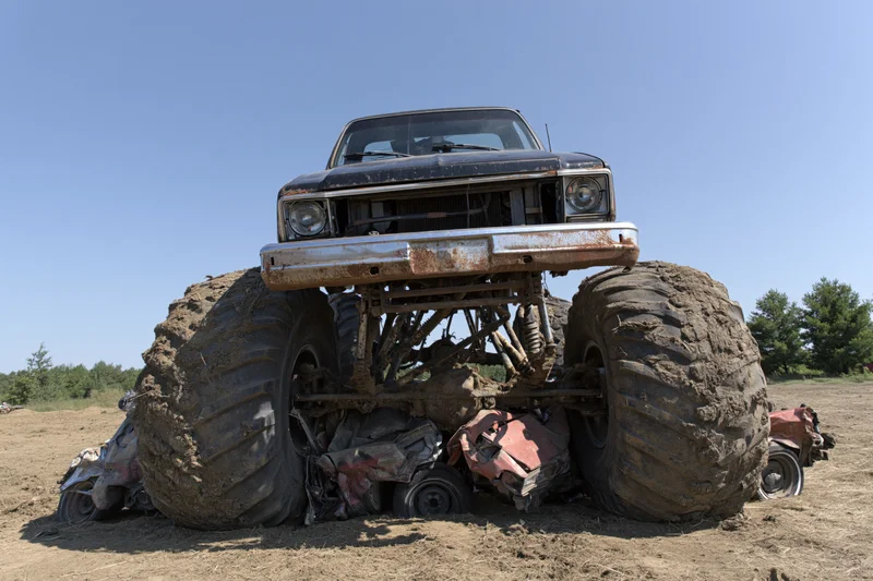Monster truck crushing wrecked cars in a dirt field under clear sky
