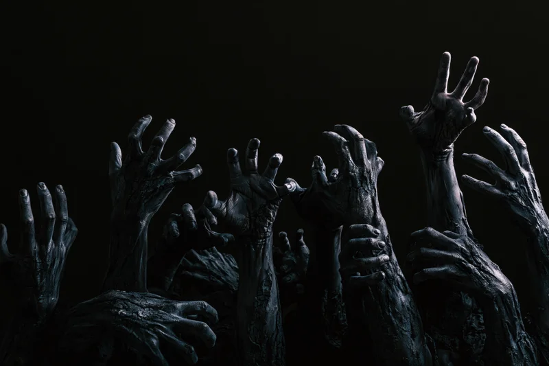 Decayed zombie hands reaching upward from darkness