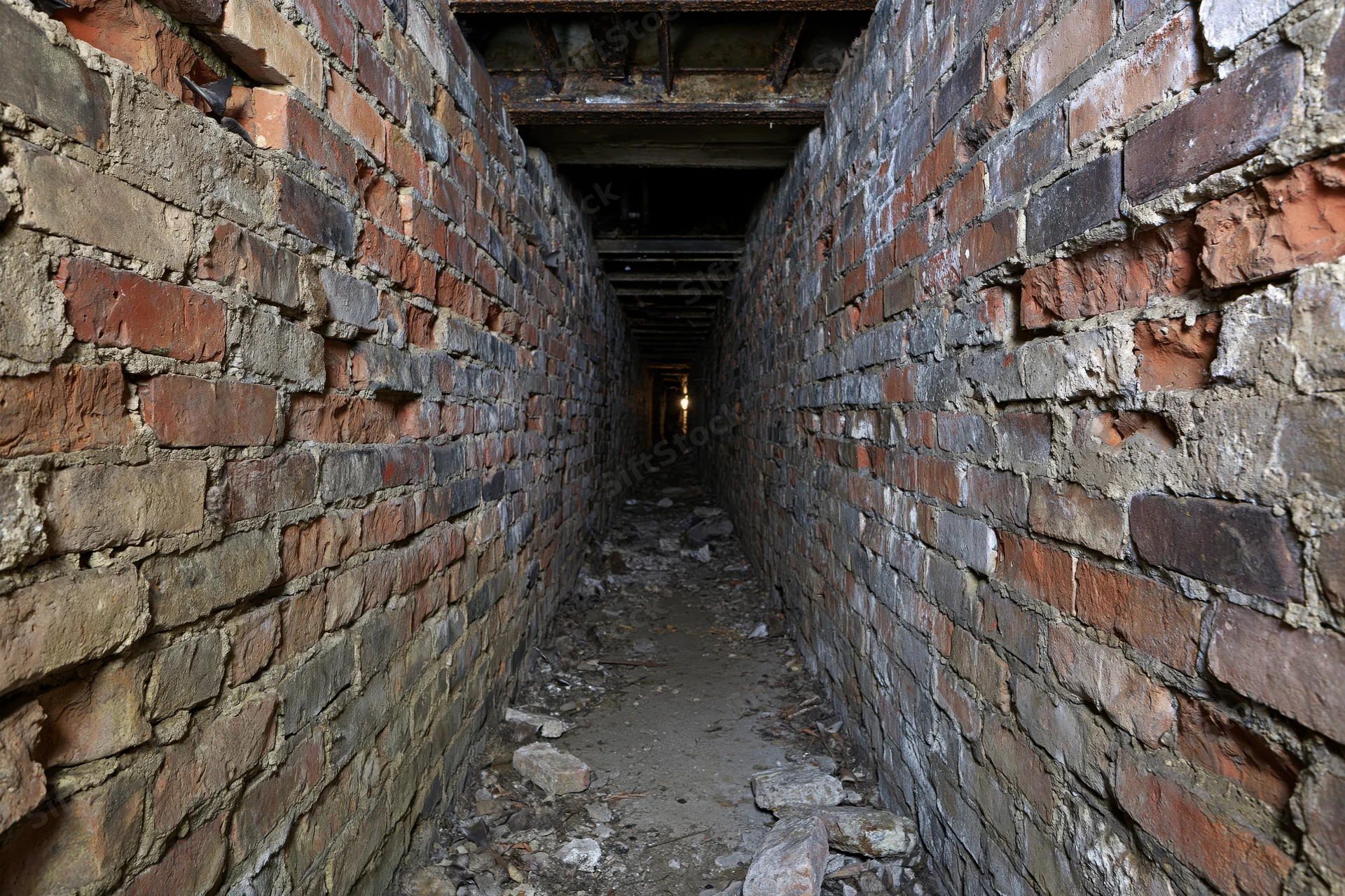 Narrow abandoned underground brick tunnel stretching into darkness with crumbling walls and debris on the floor