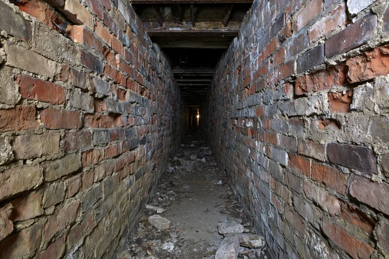 Narrow abandoned underground brick tunnel stretching into darkness with crumbling walls and debris on the floor
