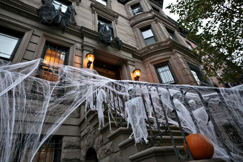 Halloween-decorated brownstone stoop with spiderwebs, skeletons, and pumpkin on railing