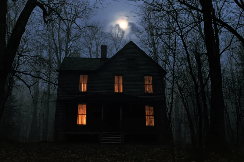 Old wooden farmhouse with glowing windows at night in a dense forest