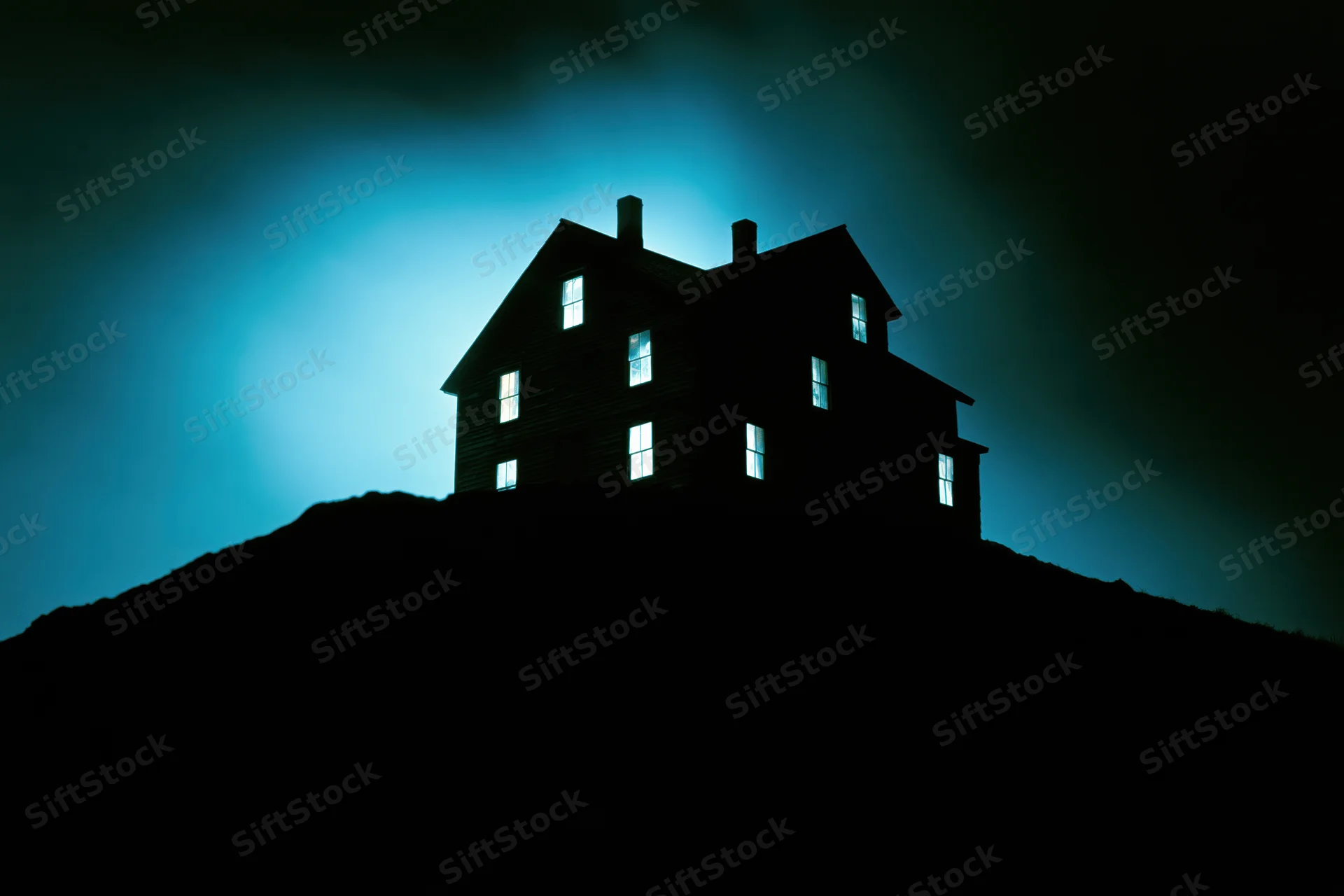 Silhouetted two-story house on a dark hill at night with glowing windows