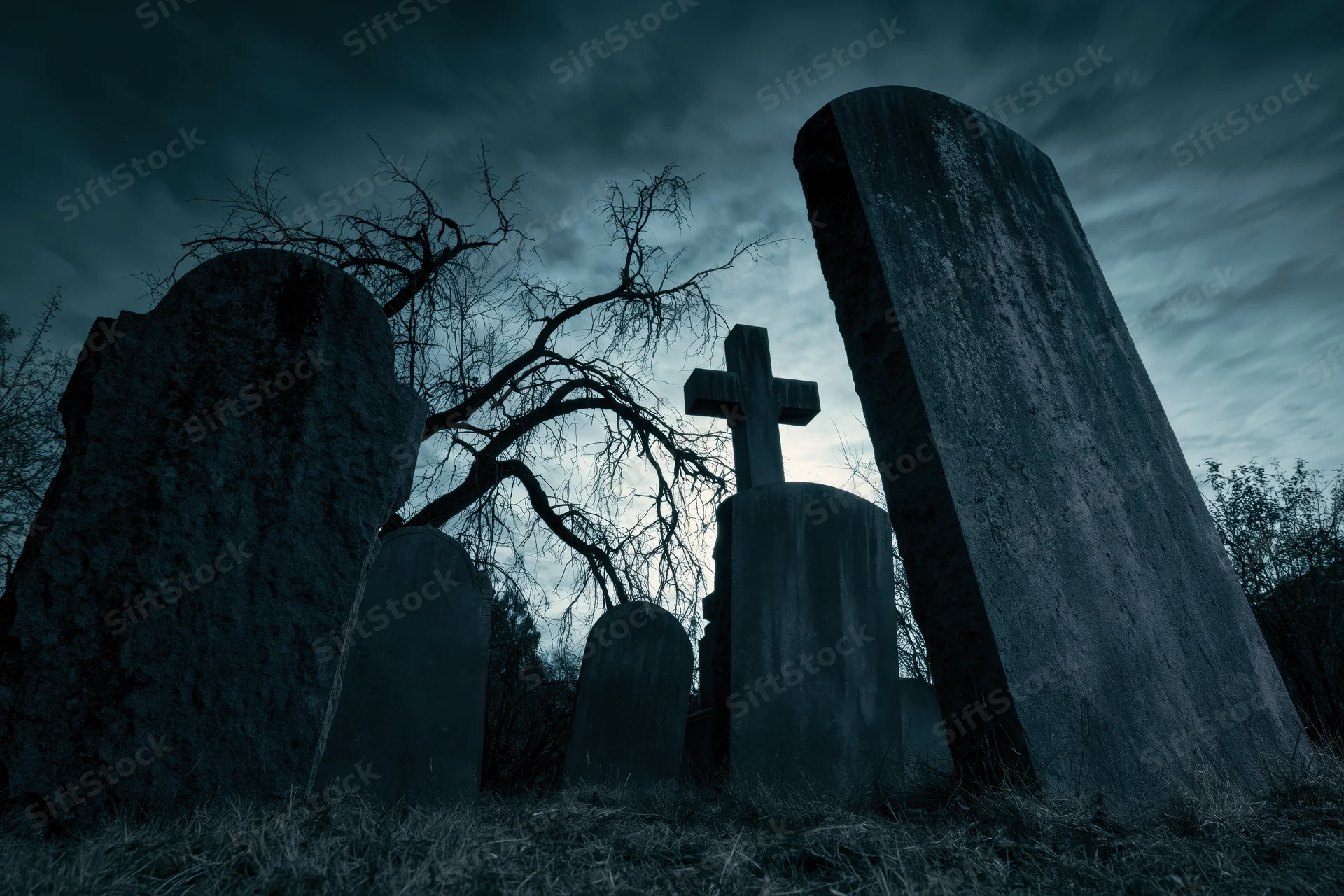Weathered gravestones and a stone cross in a dark cemetery at twilight