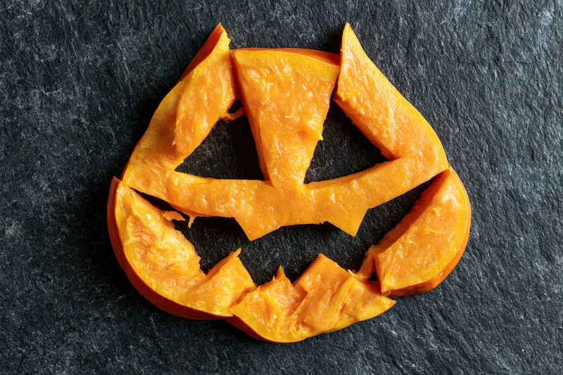 Carved pumpkin flesh pieces arranged in jack-o-lantern shape on dark slate surface