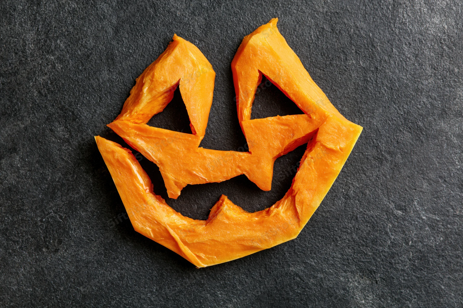 Carved pumpkin flesh arranged as a jack-o-lantern face on dark slate surface
