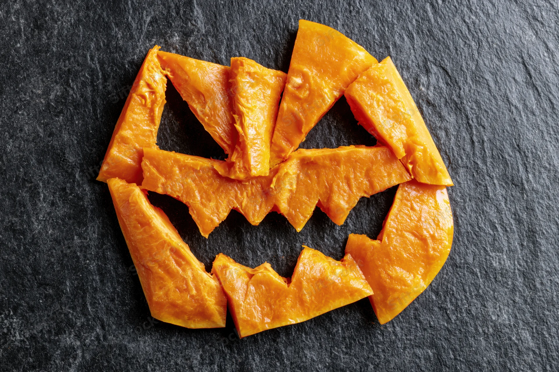 Pumpkin flesh pieces arranged in jack-o-lantern shape on dark slate surface