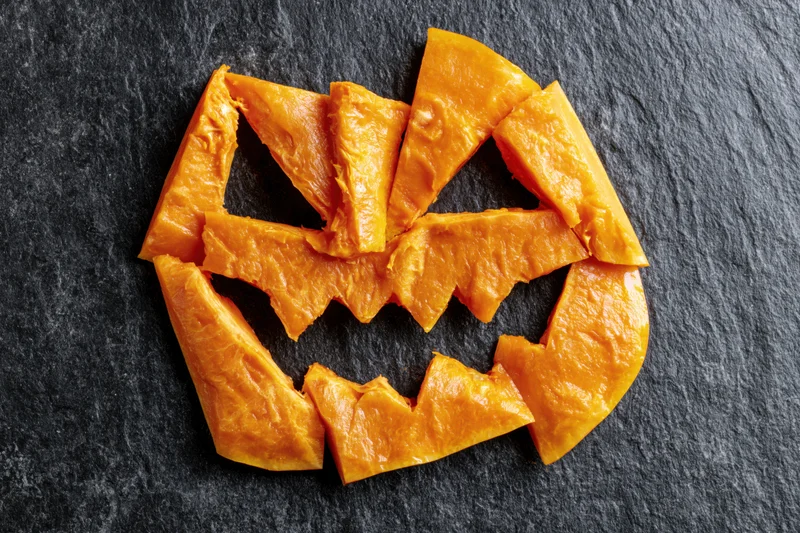 Pumpkin flesh pieces arranged in jack-o-lantern shape on dark slate surface
