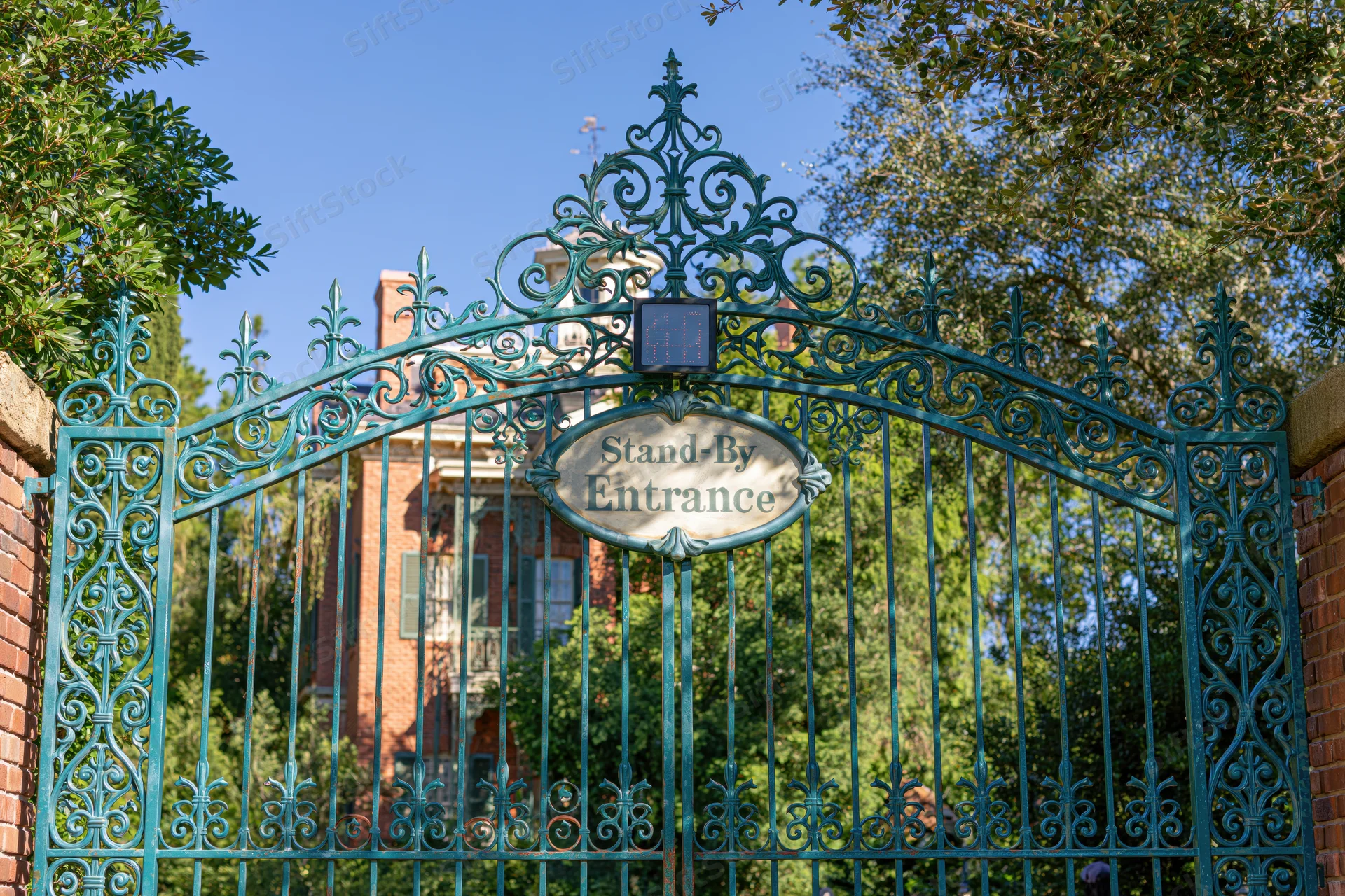 Ornate teal wrought-iron gate with standby entrance sign at haunted mansion attraction