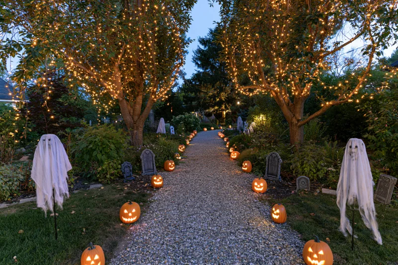 Gravel garden path lined with glowing jack-o-lanterns and ghost decorations at dusk