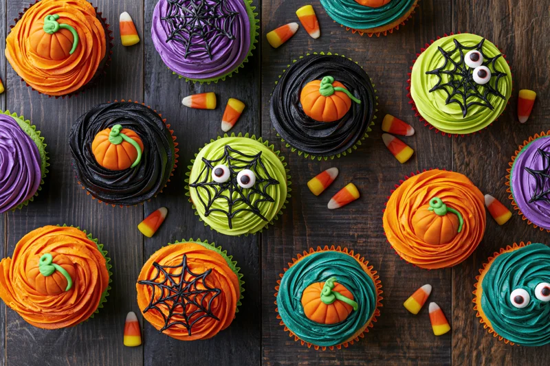 Halloween-themed cupcakes with pumpkin and spiderweb decorations arranged on a wooden surface in overhead flat lay view
