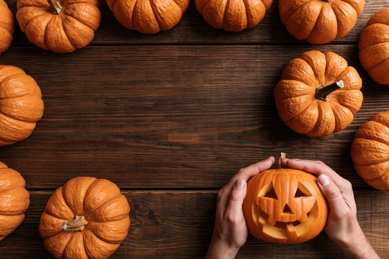 Hands holding a carved jack-o-lantern on a wooden table surrounded by pumpkins