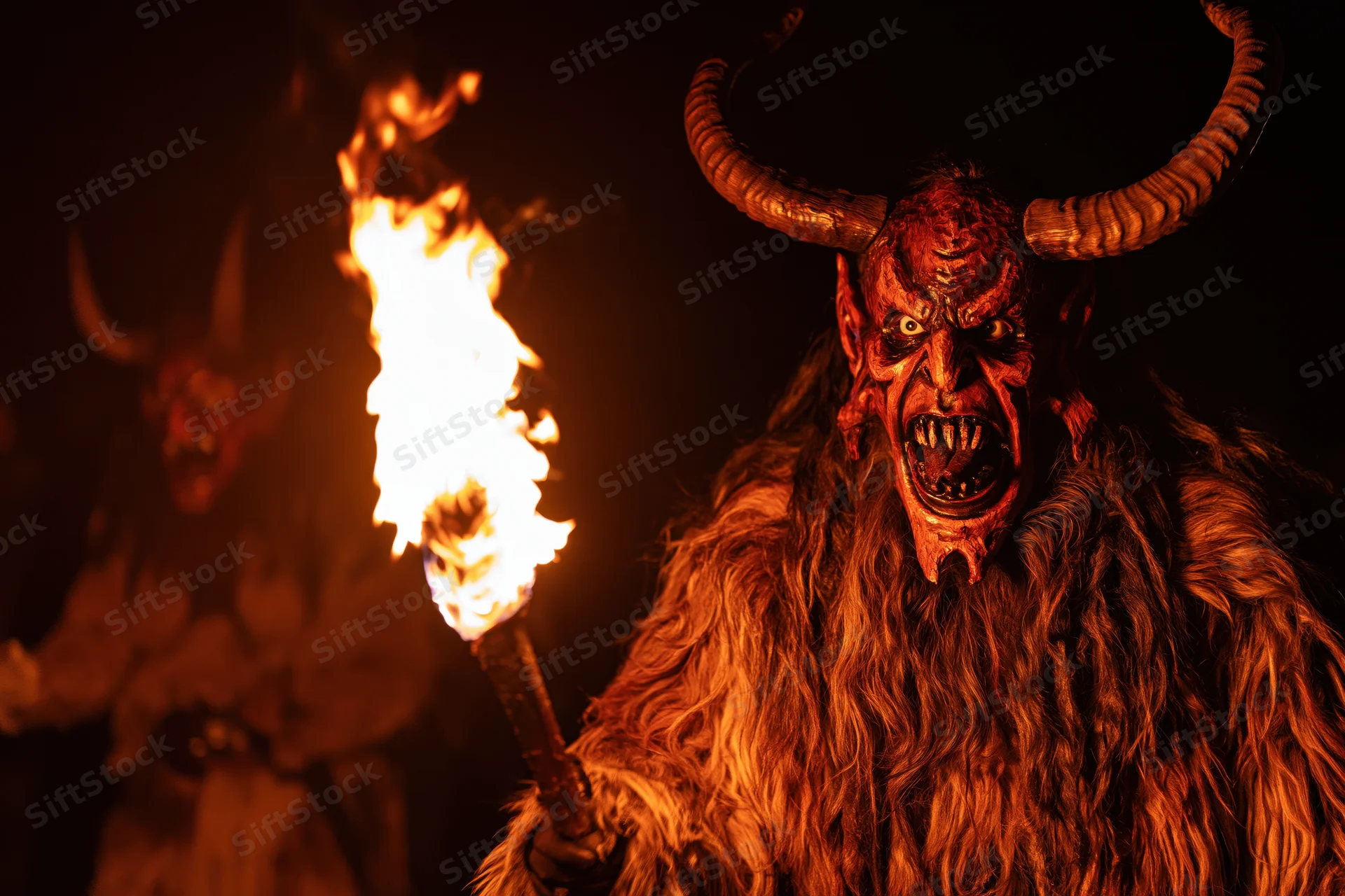 Krampus performer in traditional alpine costume holding torch at night