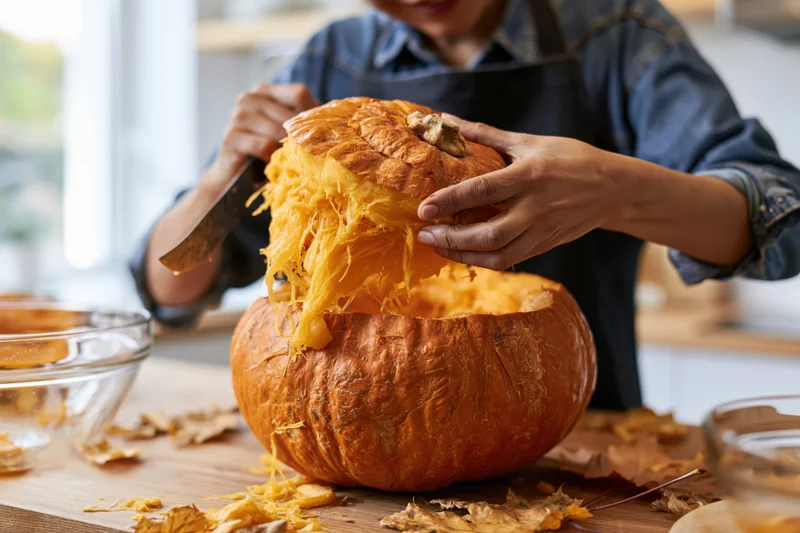 Woman carving a pumpkin on a wooden kitchen table