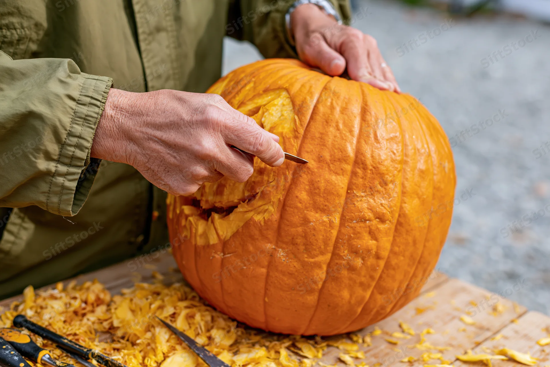 Man carving a face into a large orange pumpkin on a wooden board outdoors