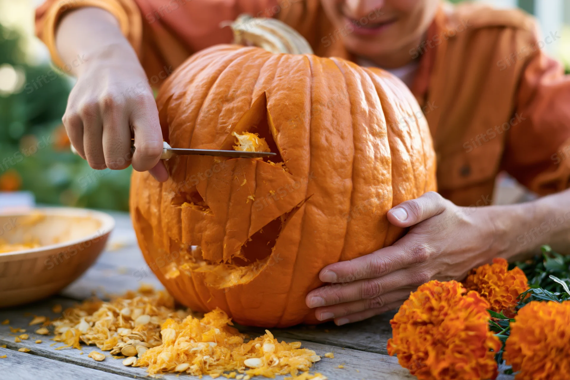 Woman carving a jack-o-lantern face into a large orange pumpkin on a wooden table outdoors