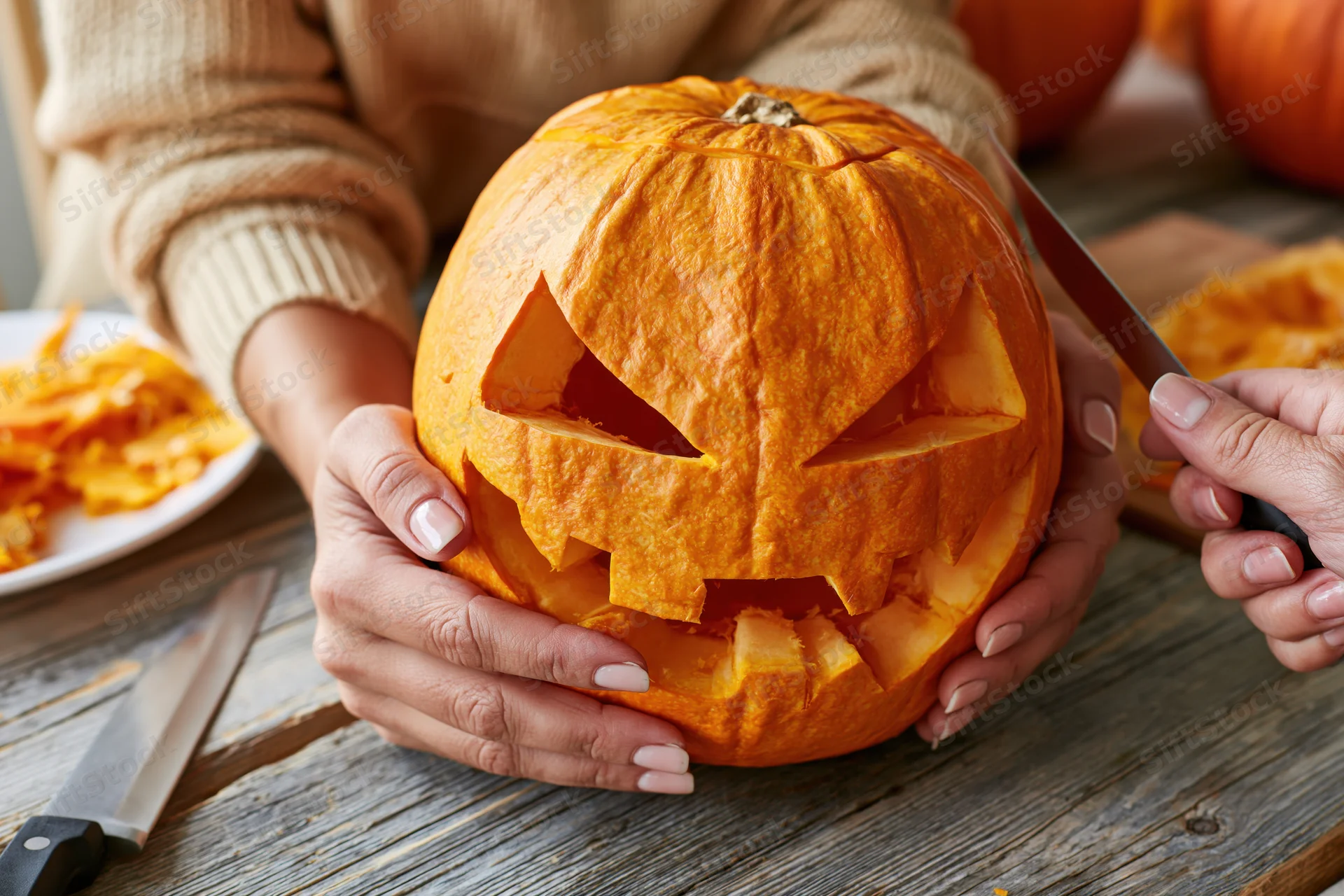 Woman carving a jack-o-lantern with a knife on a wooden table