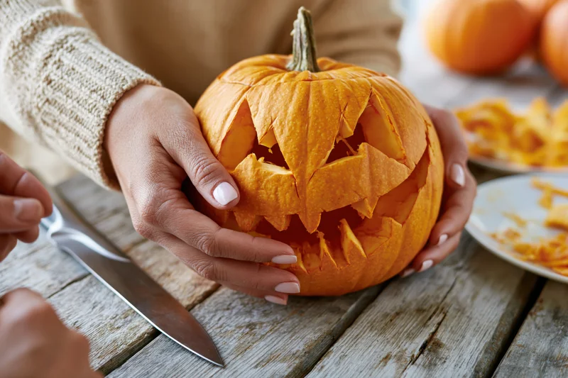 Woman holding carved jack-o-lantern on wooden table during halloween preparation