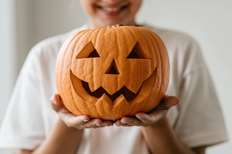 Woman holding carved jack-o-lantern in front of her face indoors
