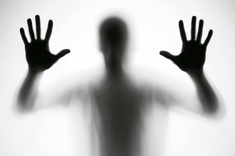 Silhouette of a man pressing hands against frosted glass, blurred figure in monochrome