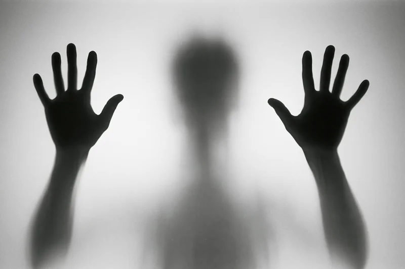 Silhouette of a person pressing hands flat against frosted glass
