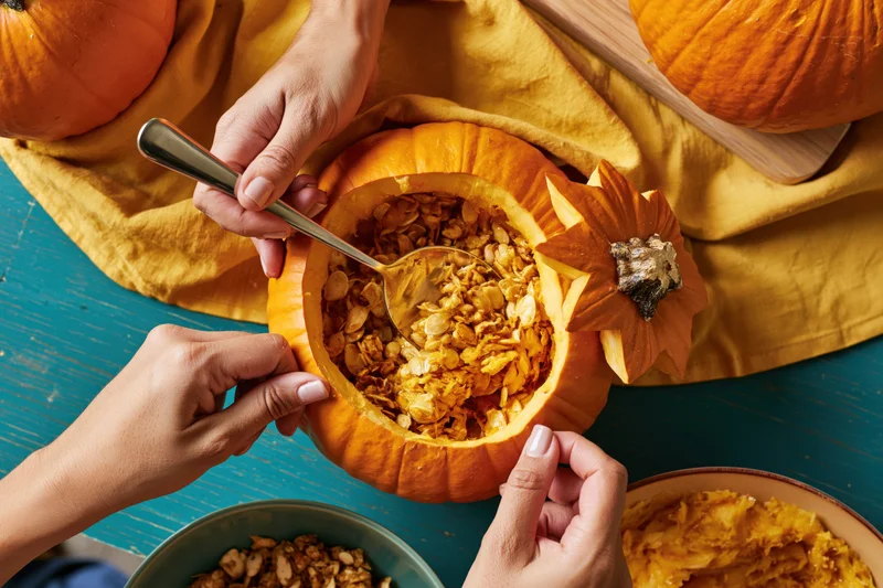 Hands scooping seeds from a carved orange pumpkin on a teal table with yellow cloth