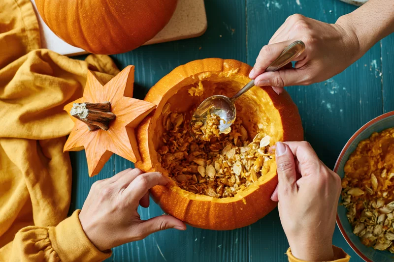 Hands scooping seeds from a carved orange pumpkin on a teal wooden table