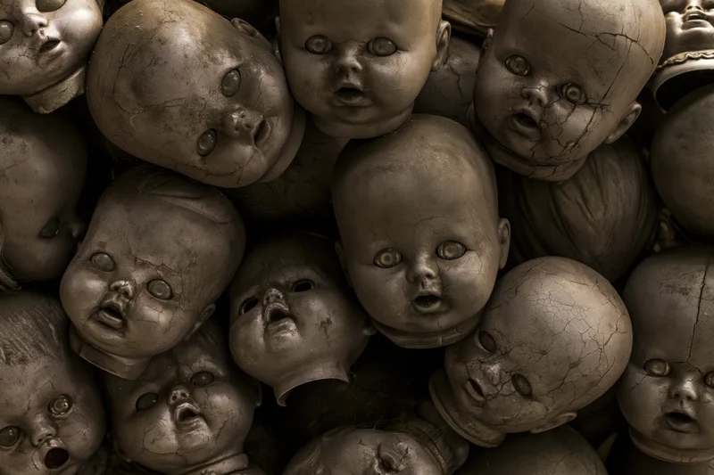 Decayed baby doll heads piled together in a heap