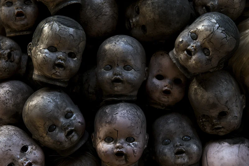 Decayed baby doll heads piled together in a dark heap