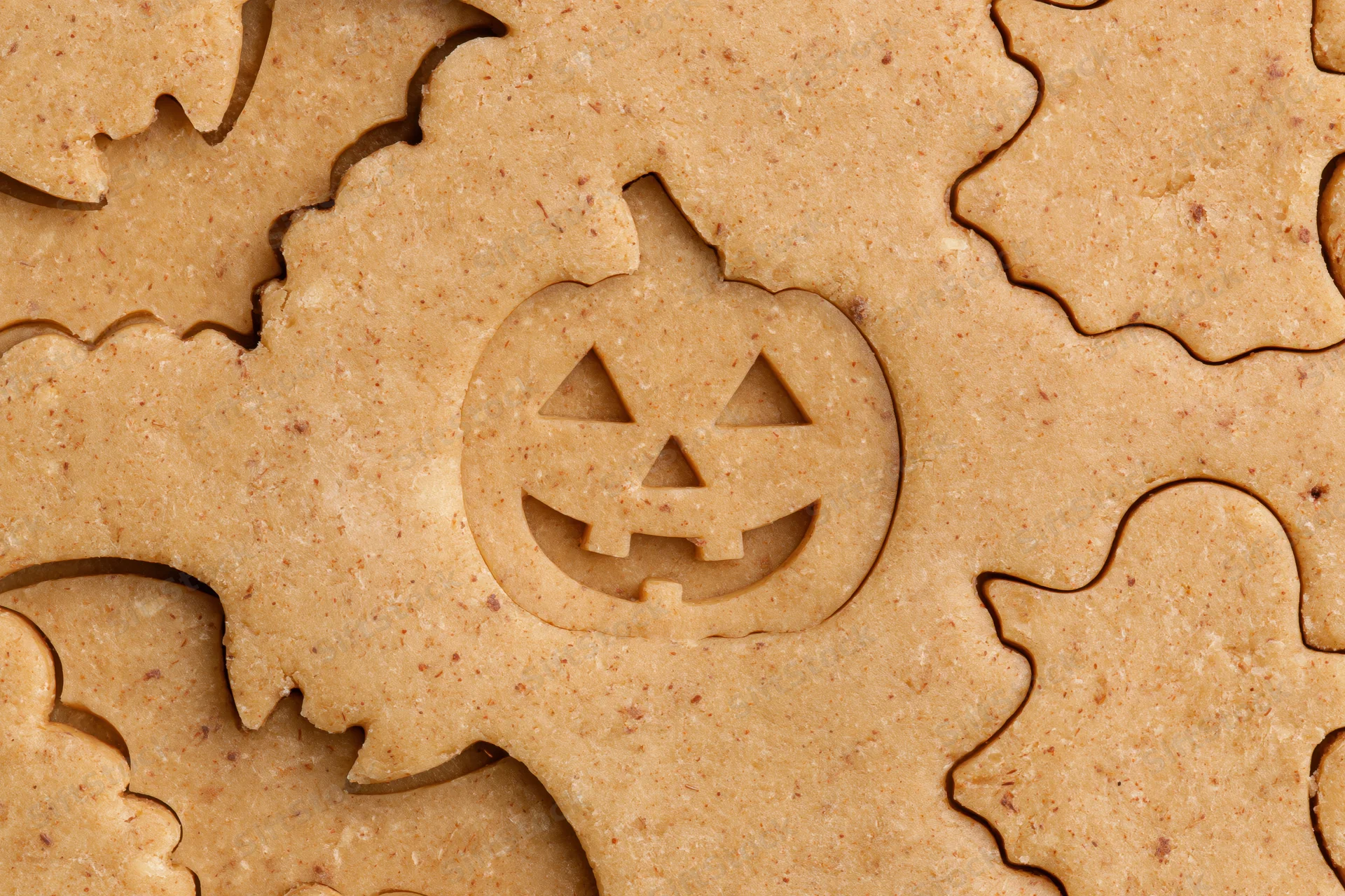 Raw gingerbread dough cut into halloween shapes including pumpkins and ghosts