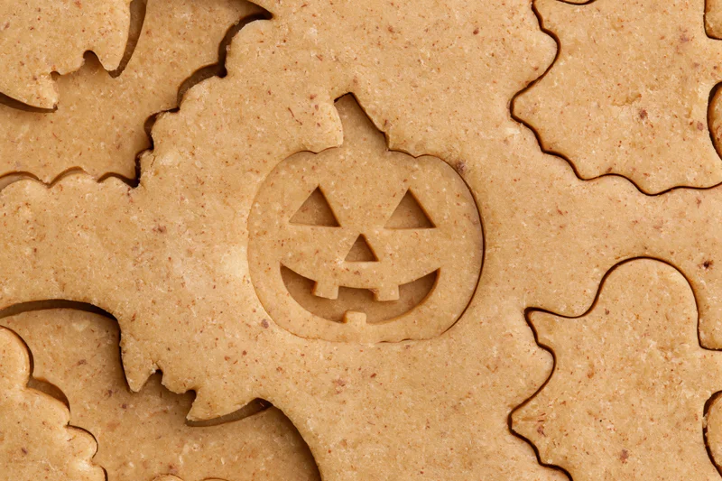 Raw gingerbread dough cut into halloween shapes including pumpkins and ghosts