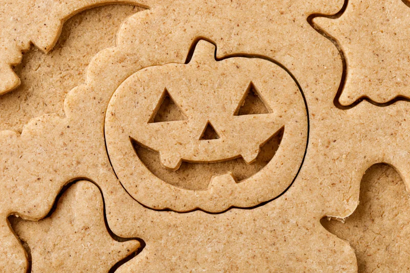 Raw gingerbread dough with halloween pumpkin cutouts arranged flat on surface