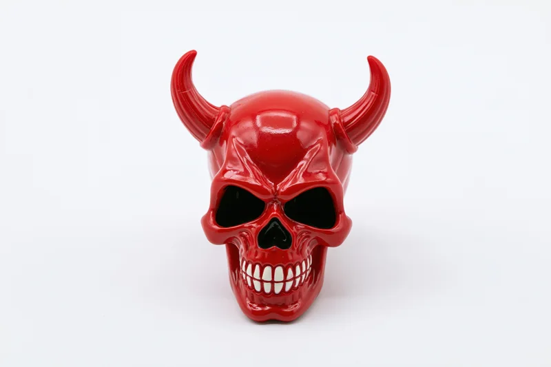 Red plastic devil skull figurine with curved horns and grinning teeth on white background