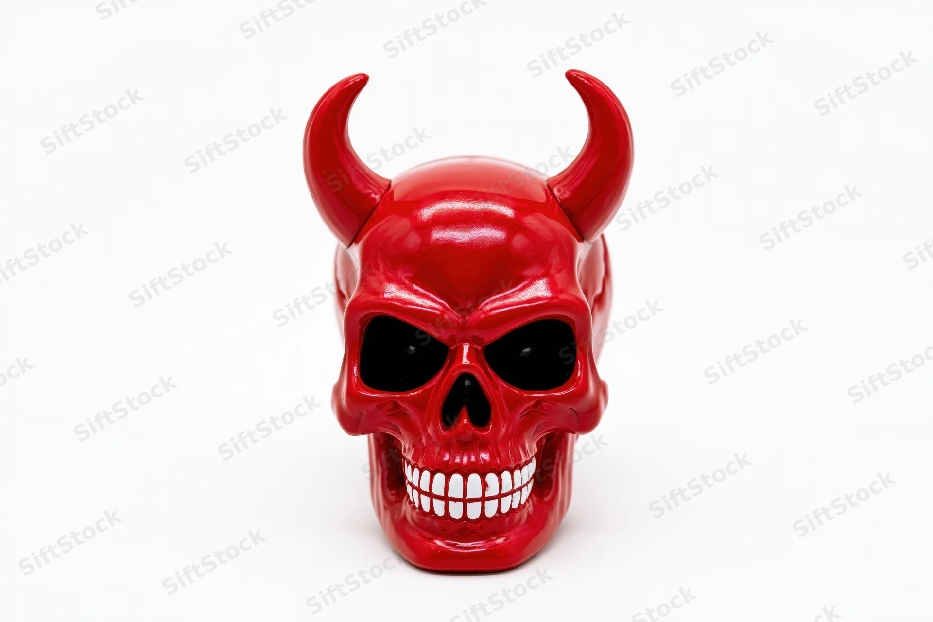 Red plastic devil skull figurine with curved horns and grinning teeth on white background