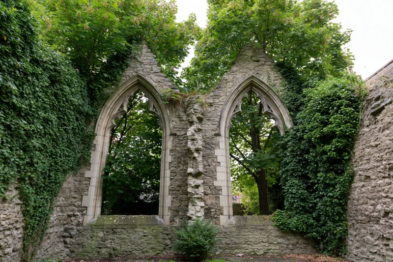 Two pointed stone arches in a roofless gothic church ruin overgrown with ivy and trees