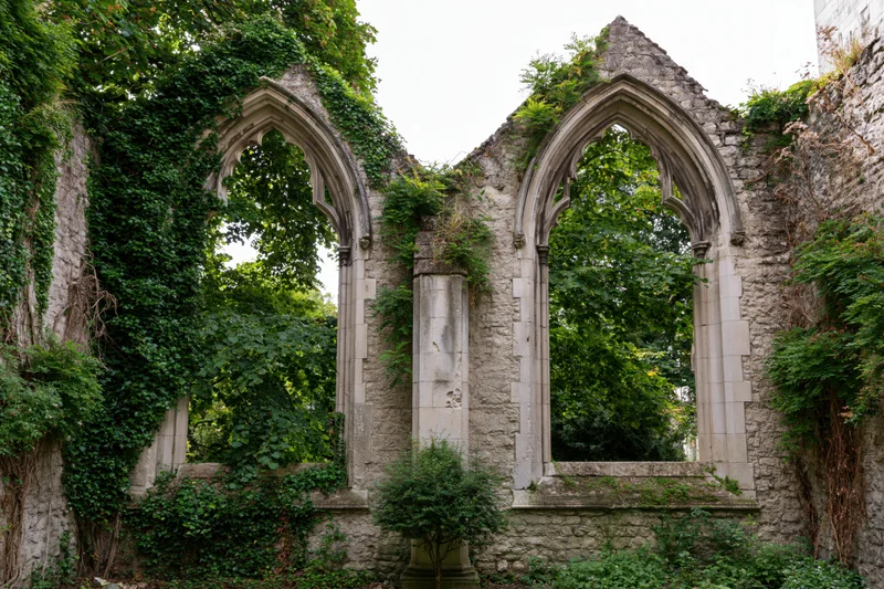 Gothic church ruin with two tall pointed stone arches overgrown with ivy and greenery