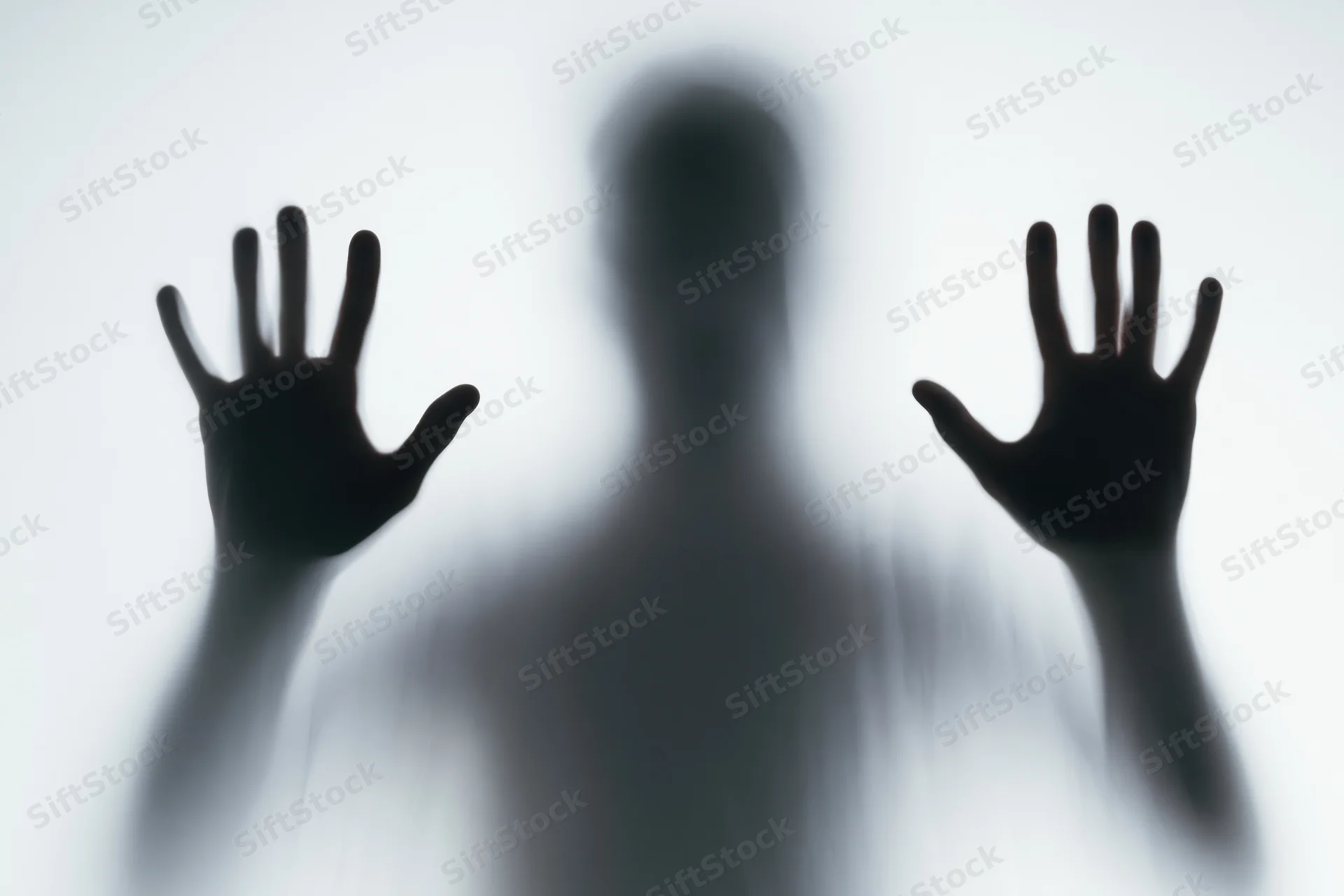 Blurred silhouette of a person pressing hands flat against frosted glass