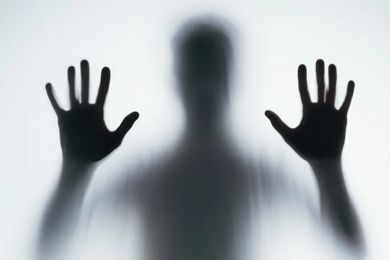 Blurred silhouette of a person pressing hands flat against frosted glass