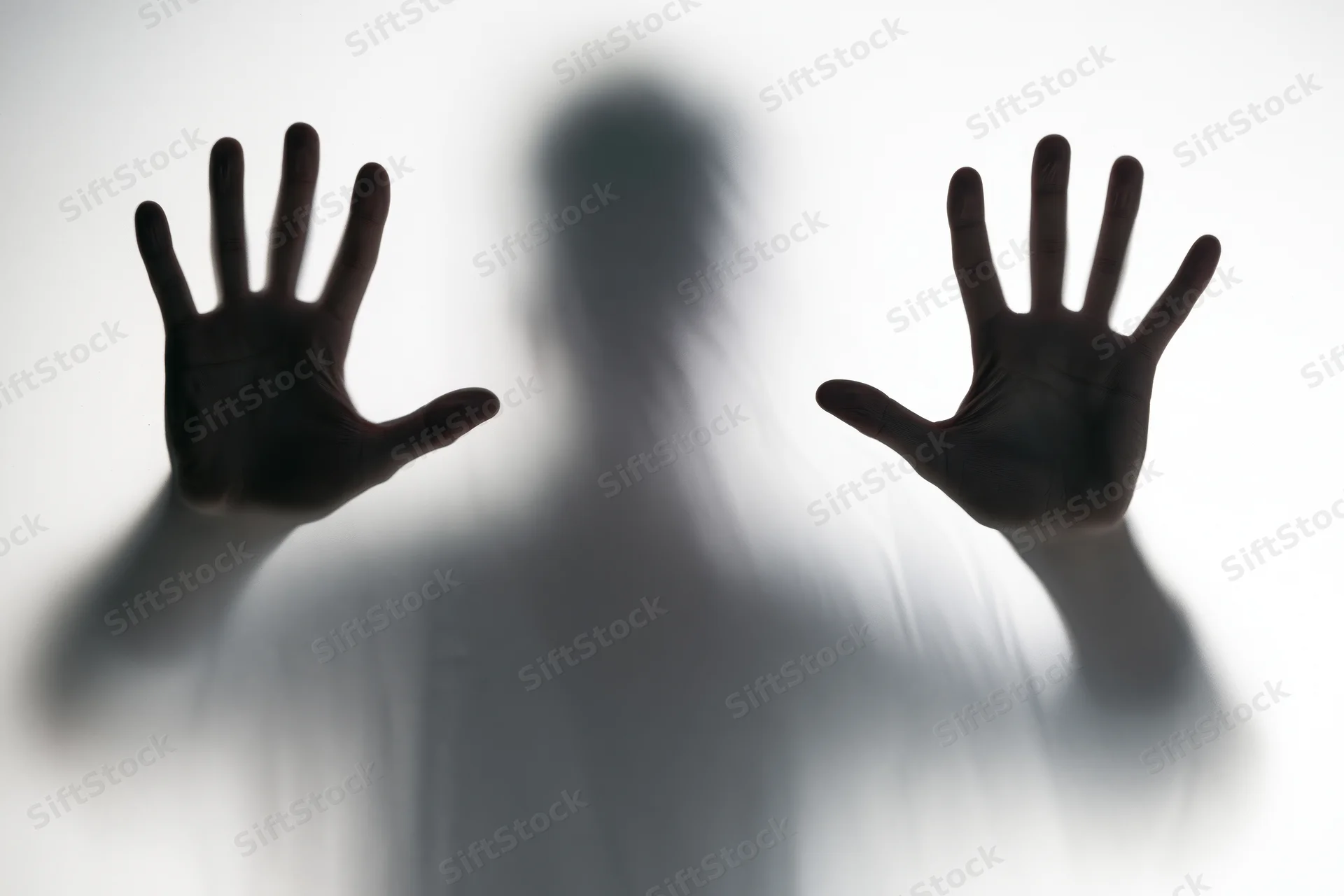 Silhouette of a person pressing hands flat against frosted glass